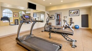 Un gimnasio con cintas de correr, elípticas y un banco.