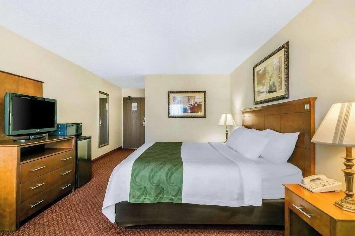 Ett hotellrum med en säng, en tv, ett skrivbord med en lampa och en tavla på väggen.