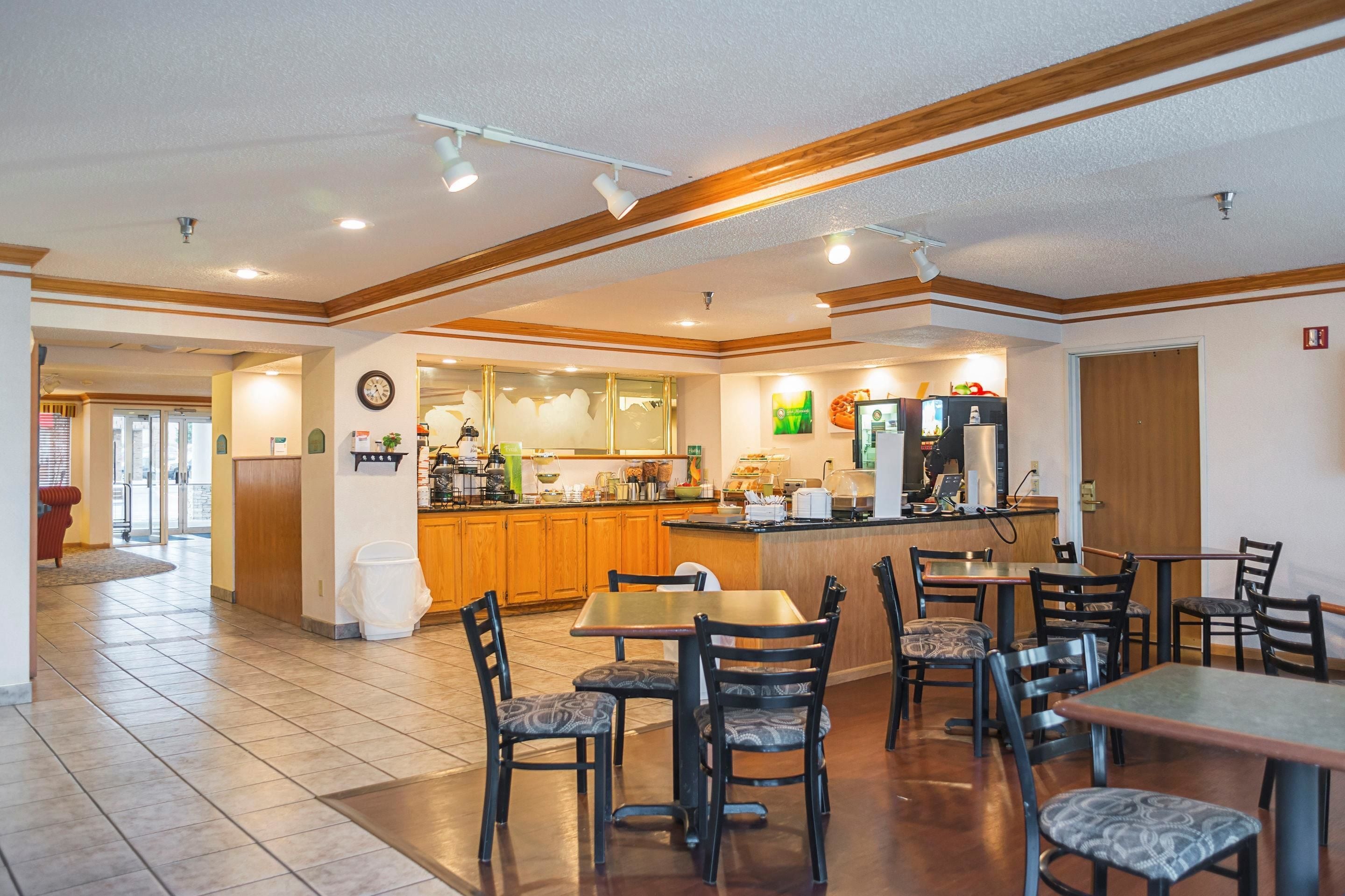 A spacious dining area with wooden tables and chairs, a kitchen in the background, and a clean, well-lit environment.