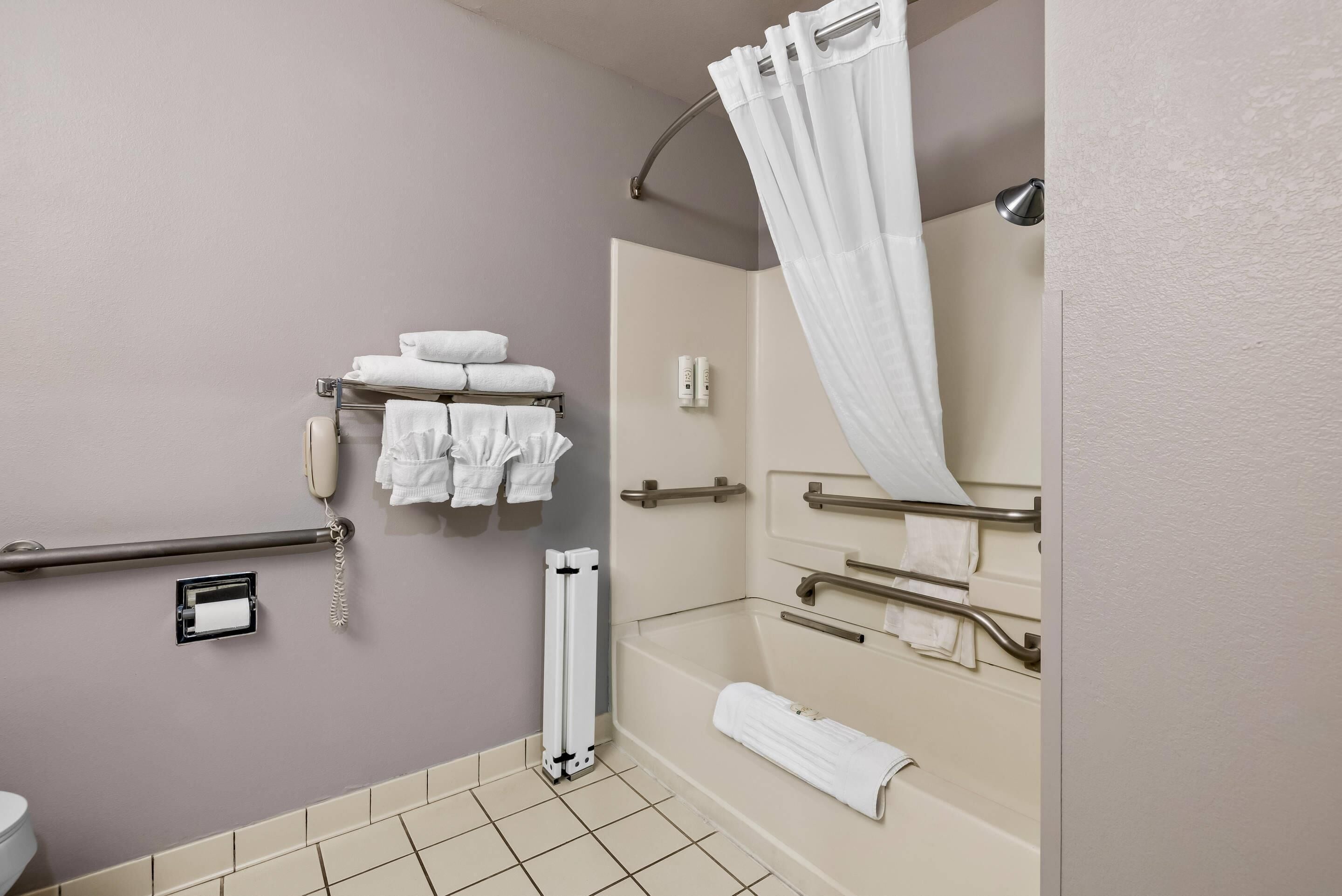 A bathroom with a toilet, a shower with a curtain, a bathtub, and a towel rack with towels.