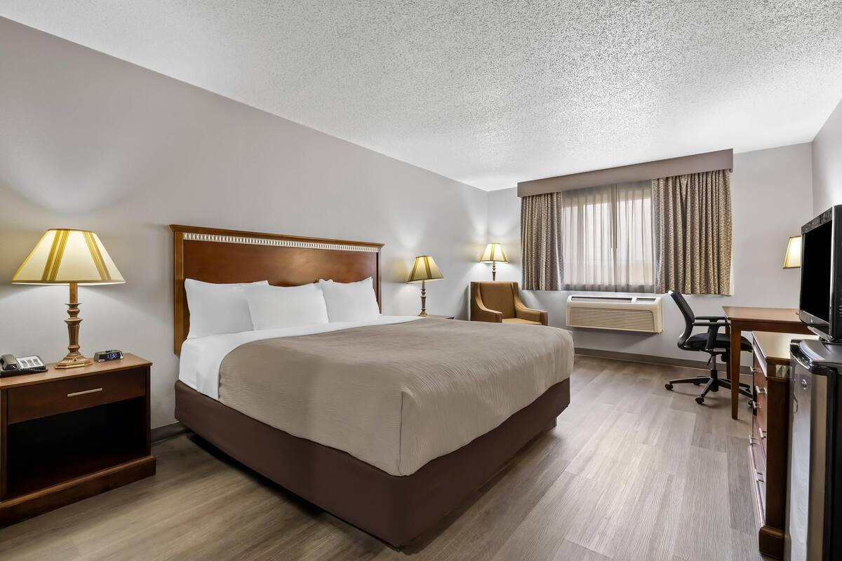 Ett hotellrum med en stor säng, sänglampor, ett skrivbord med en stol, en luftkonditioneringsanläggning och en tv.