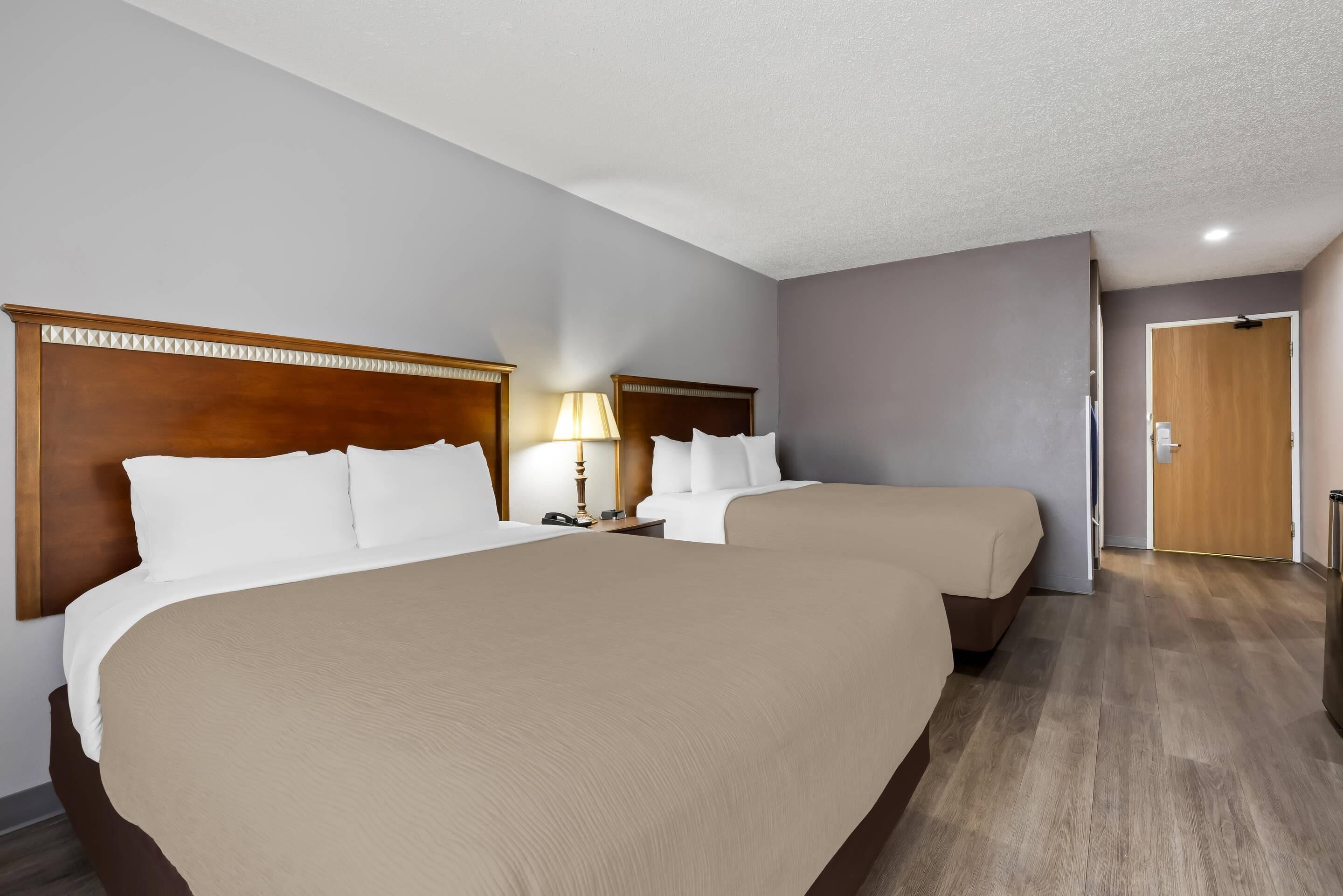 A hotel room with two beds, a wooden headboard, a nightstand with a lamp, and a wooden door.