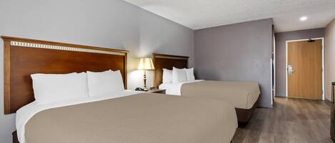 Habitación de hotel con dos camas, un cabecero de madera, una mesita de noche con lámpara y una puerta de madera.
