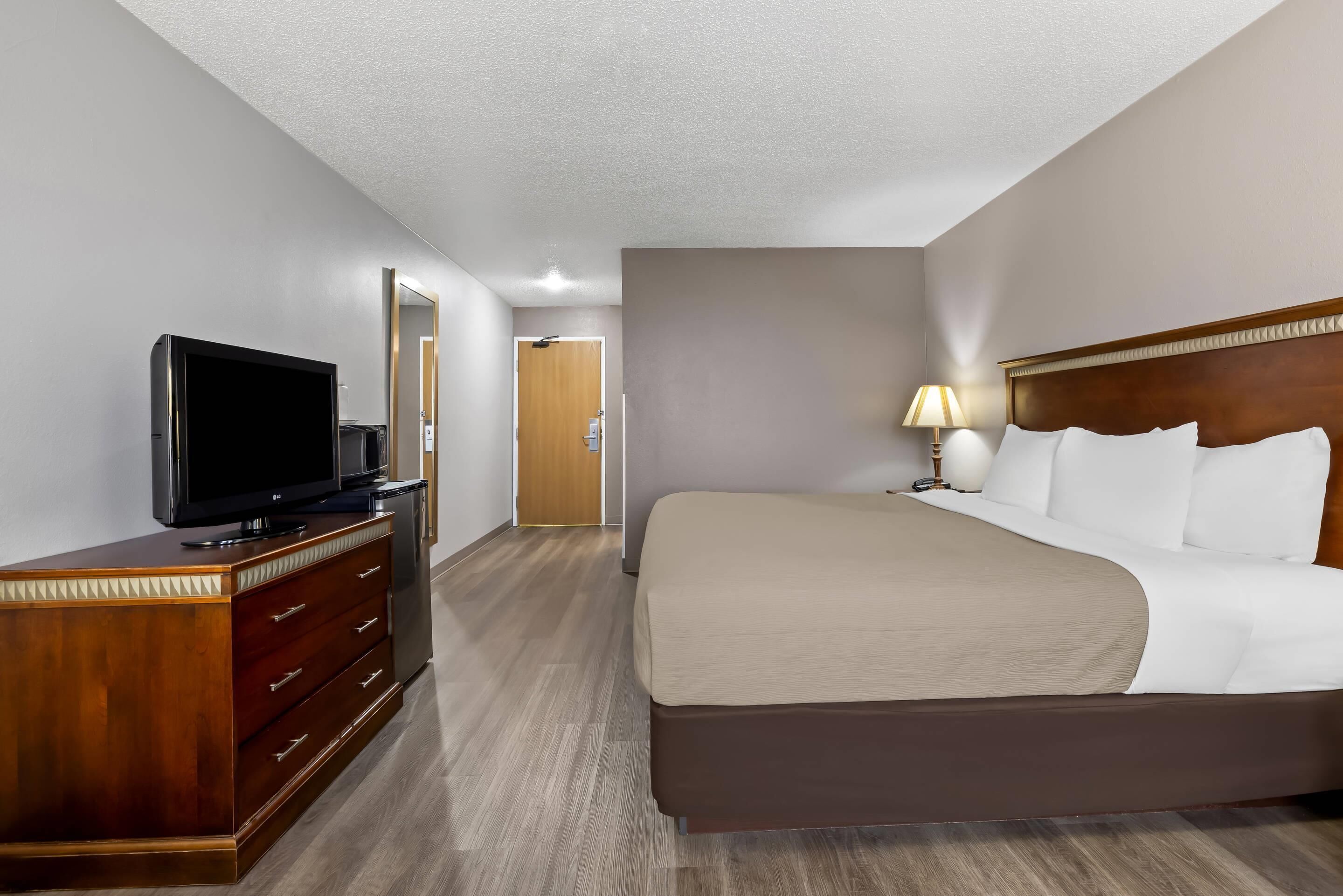 Een hotelkamer met een bed, een televisie op een houten dressoir, een lamp en een deur naar een andere kamer.