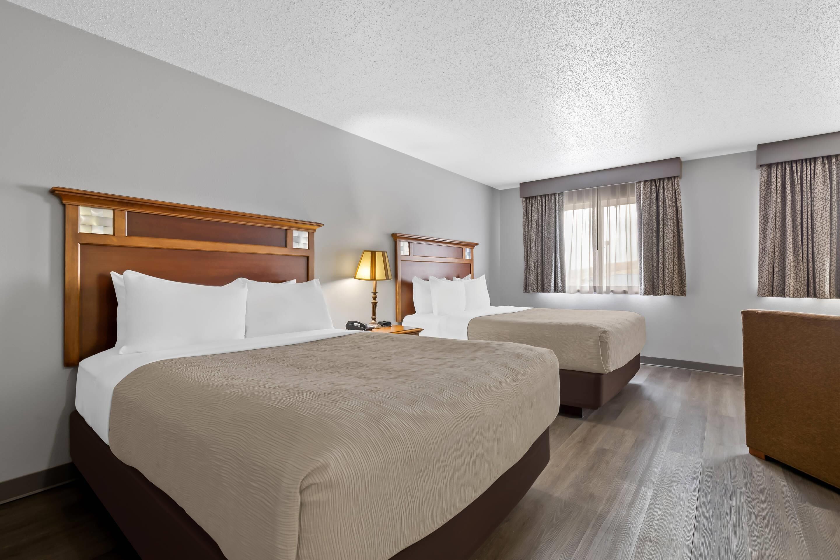 Quarto de hotel com uma cama grande, duas camas menores, uma escrivaninha e uma cadeira.