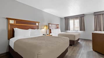 A hotel room with a large bed, two smaller beds, a desk, and a chair.