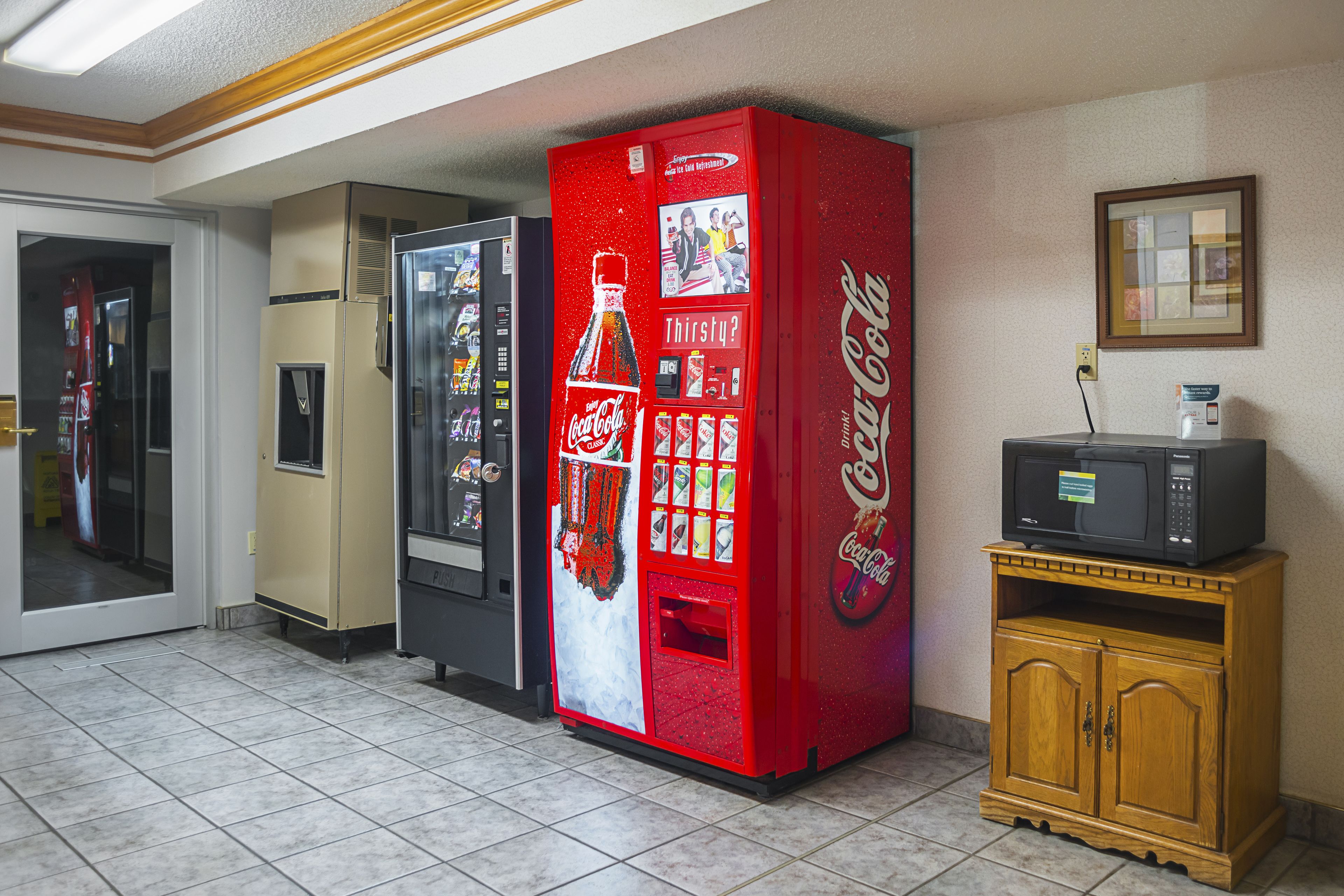 Zona con máquinas expendedoras, una máquina de Coca-Cola, un microondas sobre un mueble de madera y un refrigerador.