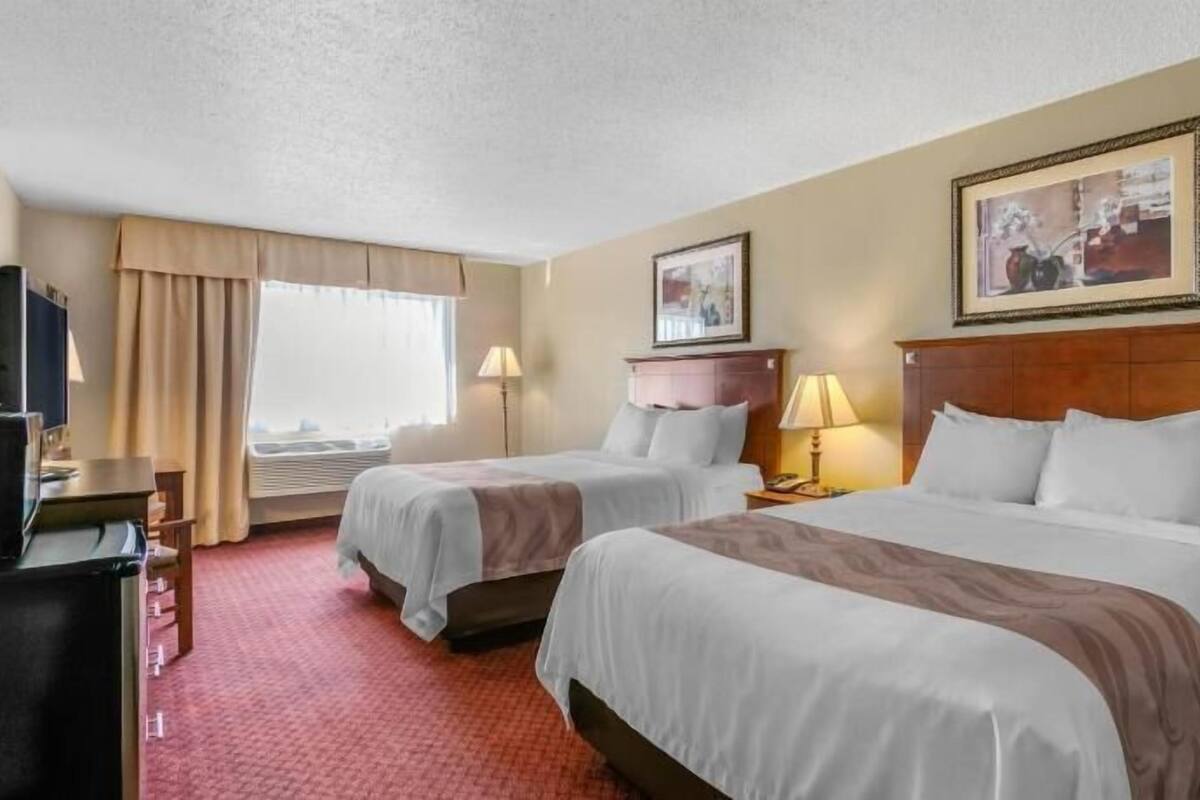 Ett hotellrum med två sängar, ett skrivbord, en tv och ett fönster med gardiner.