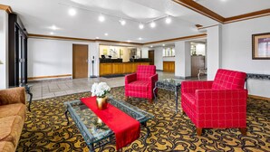 Un vestíbulo con mostrador de recepción, sillones rojos, una mesa de centro de cristal con camino de mesa rojo, alfombra estampada y vigas de madera en el techo.