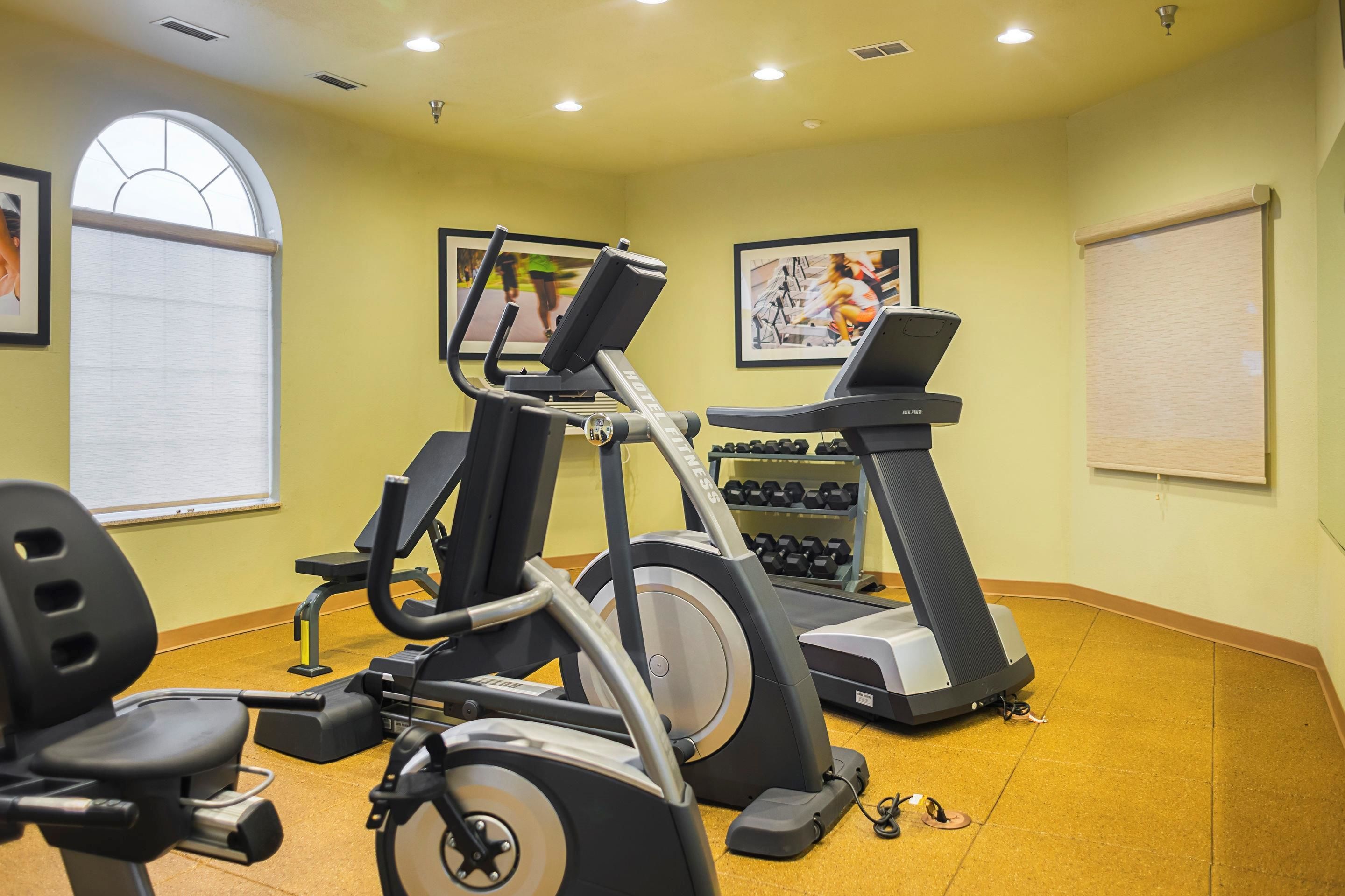 A gym with exercise equipment, including treadmills and dumbbells, and a window with blinds.