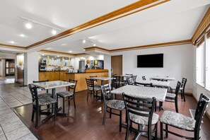 A spacious dining area with multiple tables and chairs, a kitchen in the background, and a flat-screen TV mounted on the wall. - Quality Inn near Monument Health Rapid City Hospital (Rapid City)