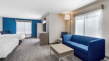 Habitación de hotel con dos camas, un sofá azul, una mesita y un amplio ventanal con cortinas.
