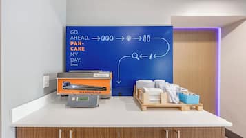 A modern kitchen area with a countertop, a blue wall with a directional sign, and a breakfast setup including a coffee maker and breakfast items.