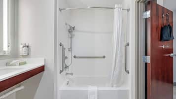 Un baño moderno con ducha a nivel, una bañera blanca y una puerta de madera.