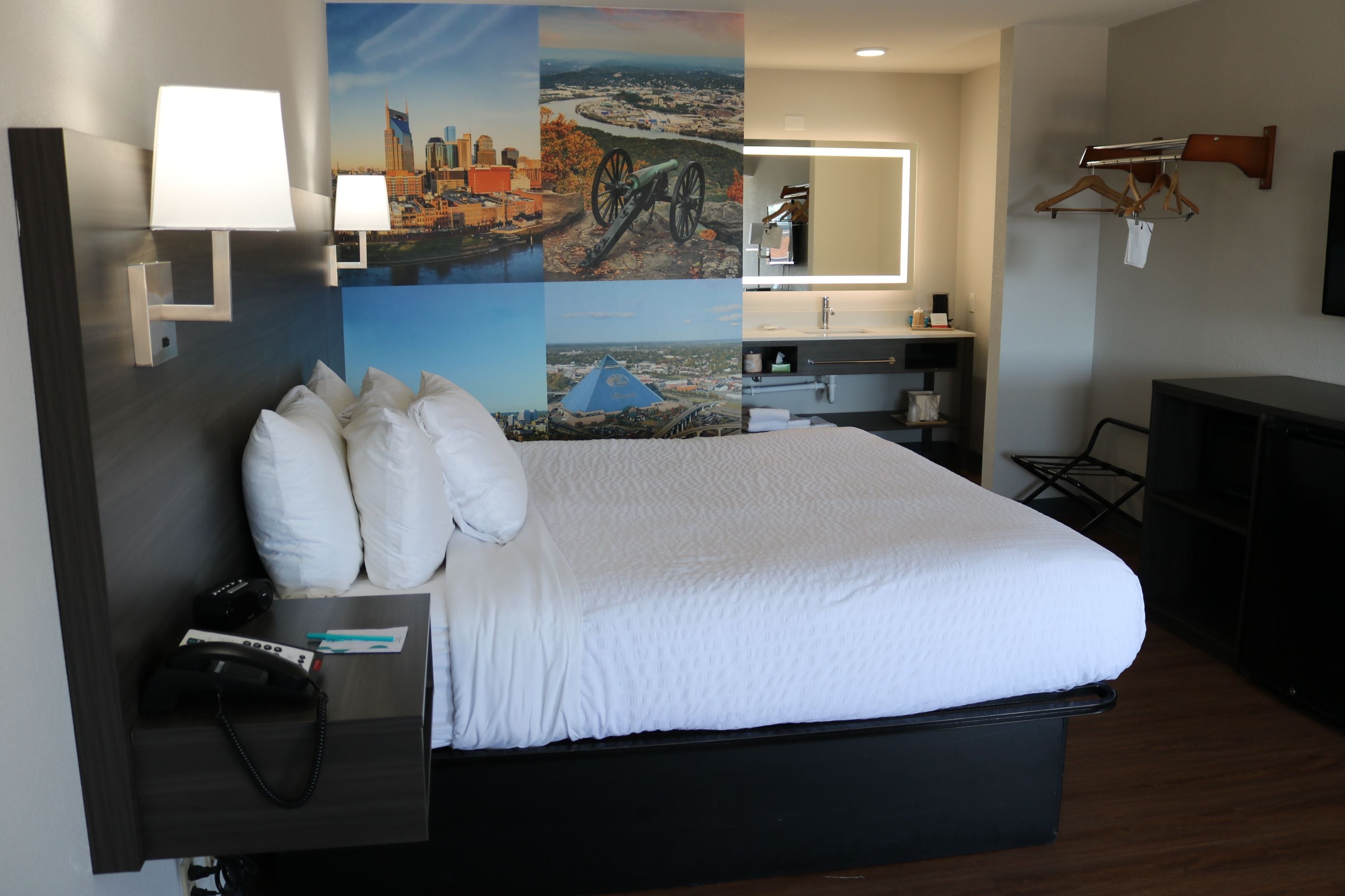 Een hotelkamer met een groot bed, een bureau met telefoon, een spiegel en een muur met een stadsgezicht muurschildering.