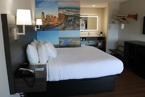 A hotel room with a large bed, a desk with a telephone, a mirror, and a wall with a cityscape mural. - Clarion Pointe (La Vergne)