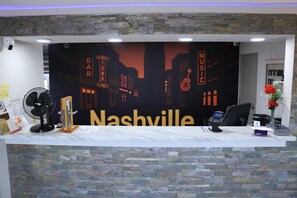 A reception desk with a cityscape mural, a fan, a phone, and a vase with flowers. - Econo Lodge Inn & Suites Southeast (La Vergne)