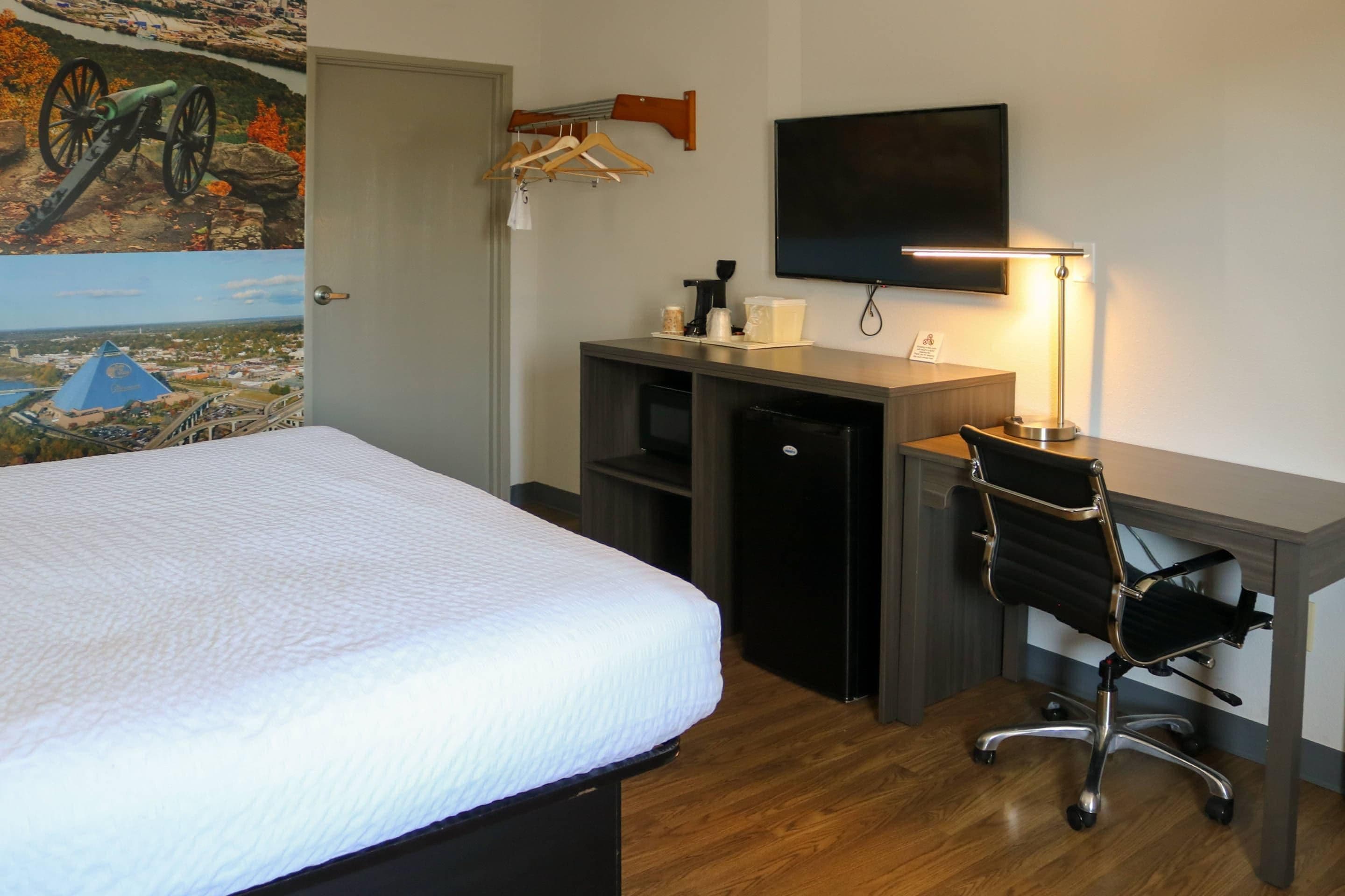 A hotel room with a bed, desk, chair, and a television.