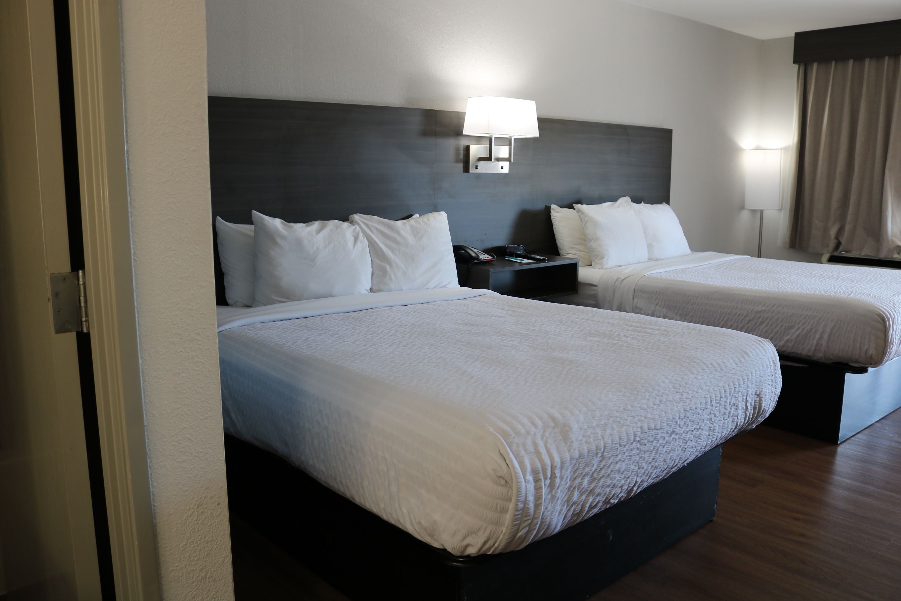 A hotel room with two beds, a nightstand with a lamp, and a wall-mounted phone.