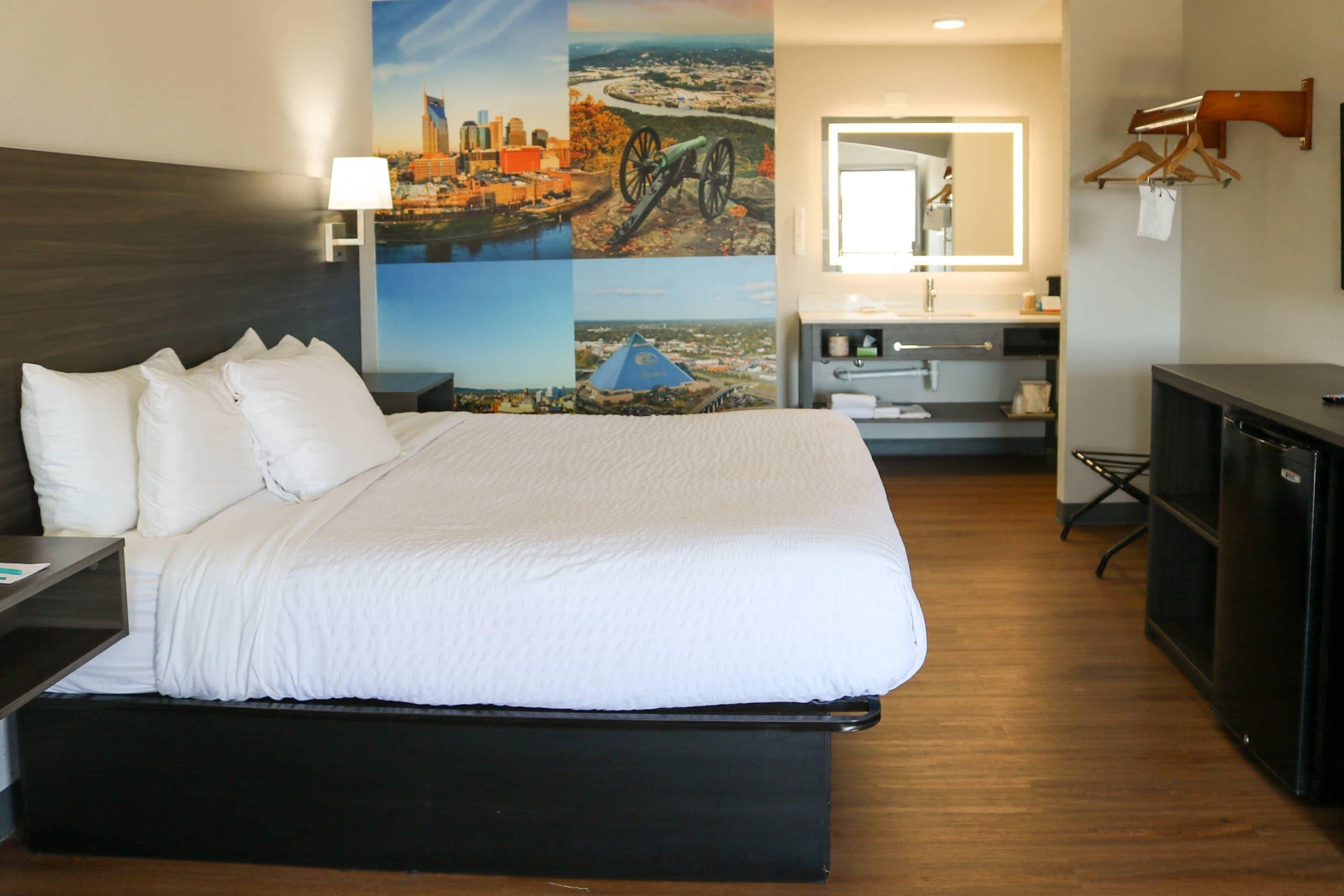Habitación de hotel con una cama grande, un escritorio, un aparador, un espejo y una pared con un mural de un paisaje urbano.