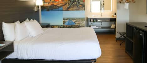 Habitación de hotel con una cama grande, un escritorio, un aparador, un espejo y una pared con un mural de un paisaje urbano.