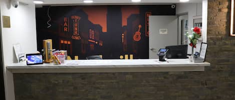 A reception desk with a cityscape mural, a computer, and a vase with flowers.