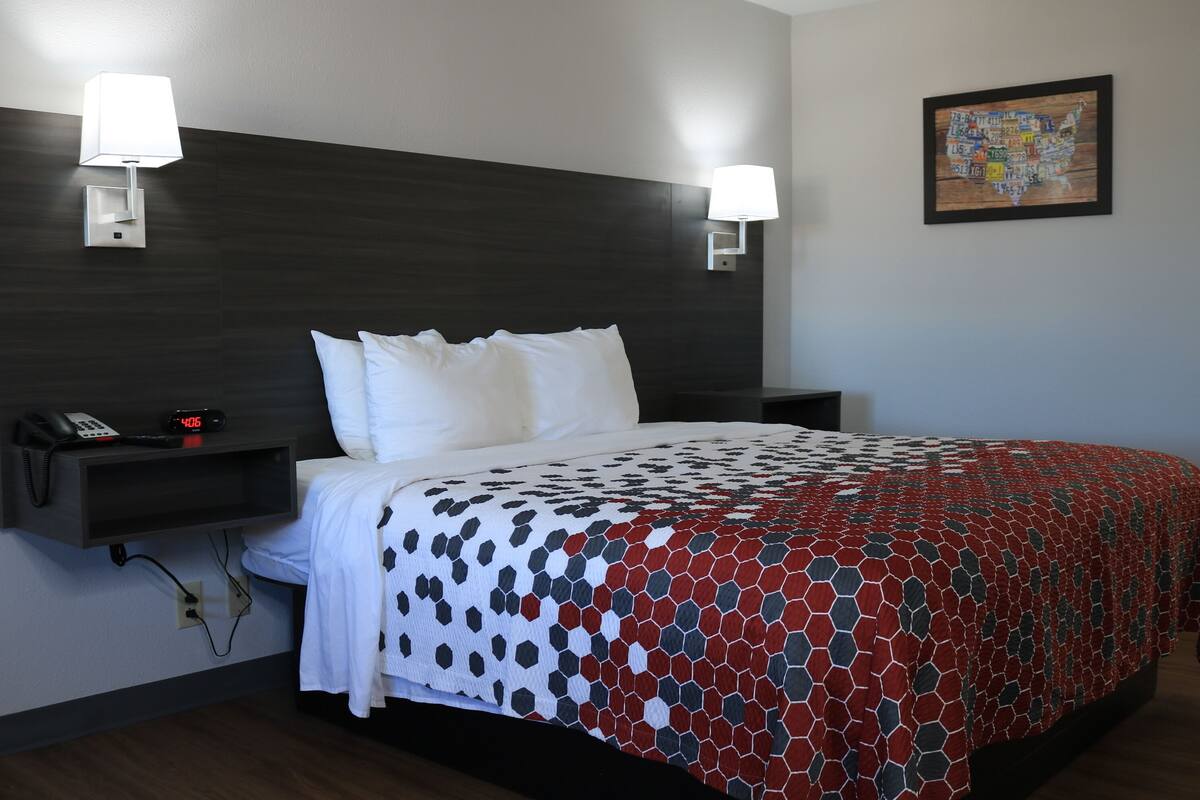 A hotel room with a large bed, two bedside lamps, a nightstand with a phone, and a wall-mounted clock.