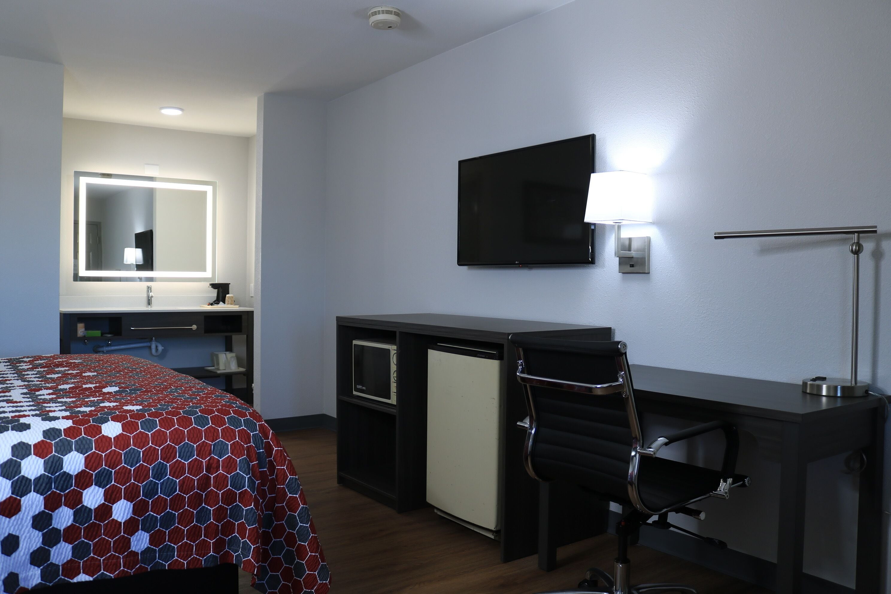 A hotel room with a bed, a desk, a chair, a television, and a mirror.