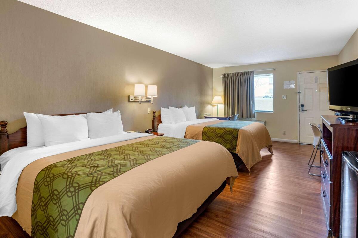 A hotel room with two beds, a television, a desk, and a window with curtains.