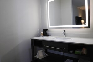 Une salle de bain moderne avec un lavabo blanc, un meuble-lavabo foncé et un miroir doté d’un éclairage à LED.