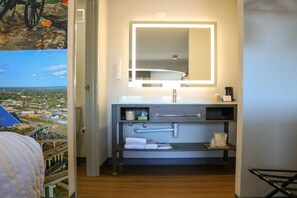 A hotel bathroom with a large mirror, a sink, and a towel rack. - Clarion Pointe (La Vergne)
