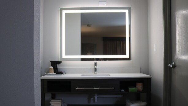 A bathroom with a white sink, a mirror with a light, and a towel rack. - Econo Lodge Inn & Suites Southeast (La Vergne)