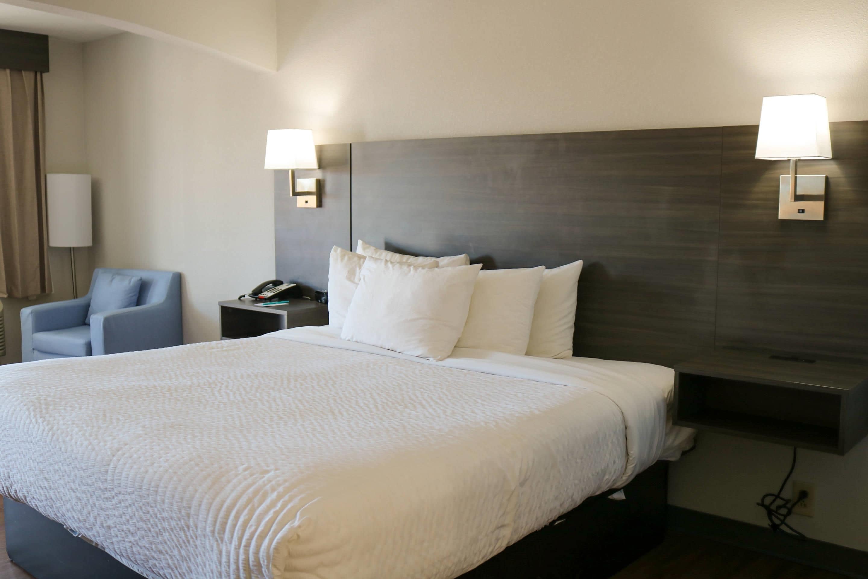 A hotel room with a large bed, two bedside lamps, a chair, a nightstand with a phone, and a wall-mounted TV.
