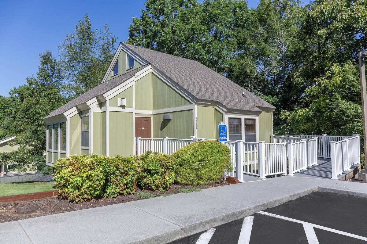 A single-story building with a sloped roof, a front entrance with a white picket fence, and a blue handicap parking sign.