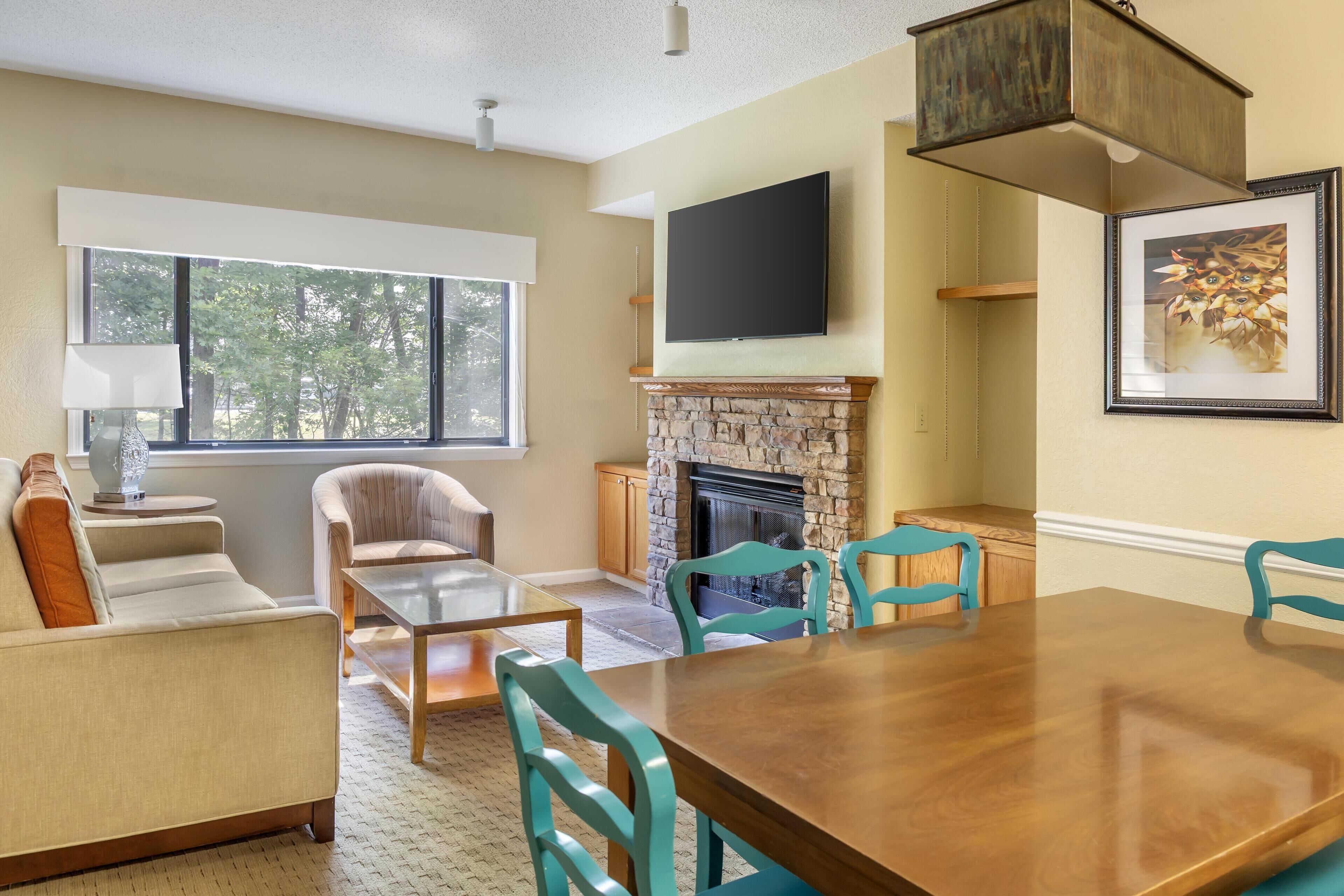 A spacious living room with a fireplace, a large flat-screen TV, and a dining area with a wooden table and chairs.