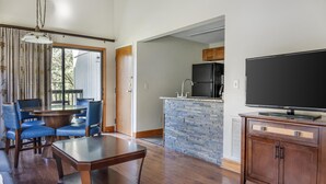 Una sala de estar moderna con comedor, una cocina con isla de piedra y un televisor de pantalla plana sobre un mueble de madera.