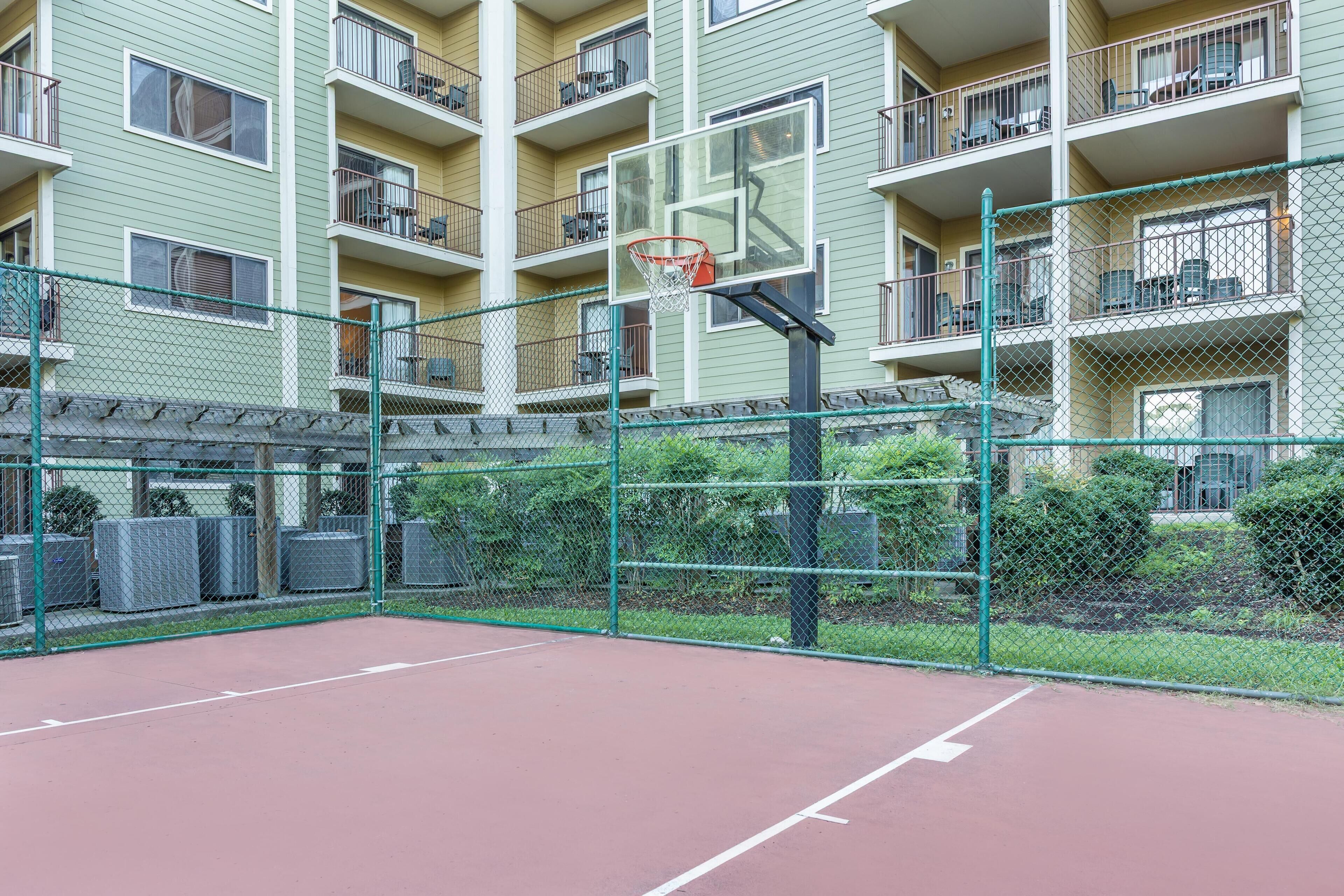 Ein Basketballplatz im Freien, umzäumt von einem Maschendrahtzaun, mit einem Korb in der Mitte.