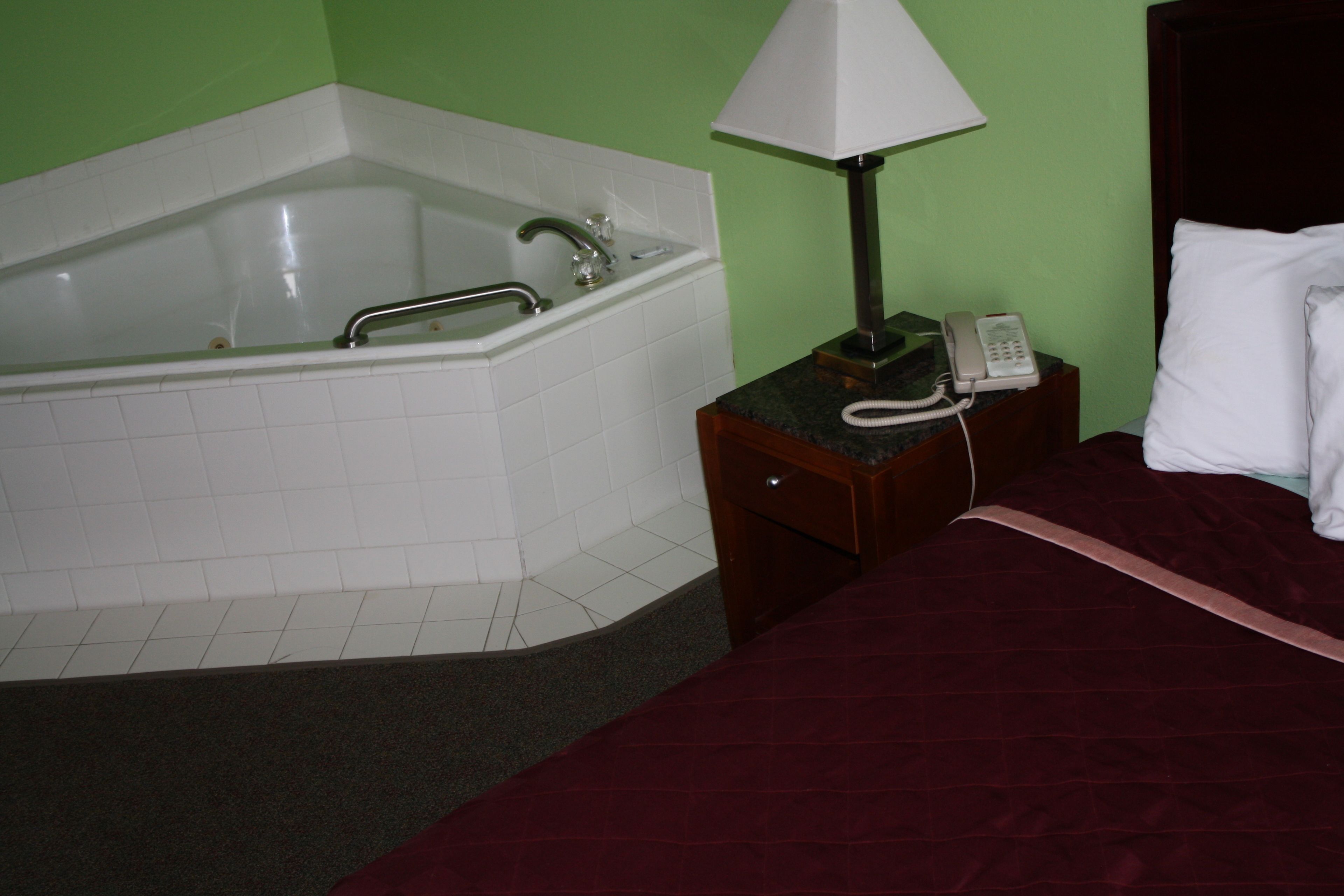 Habitació d'hotel amb banyera, una làmpada de nit, un telèfon i un llit amb llençol vermell.