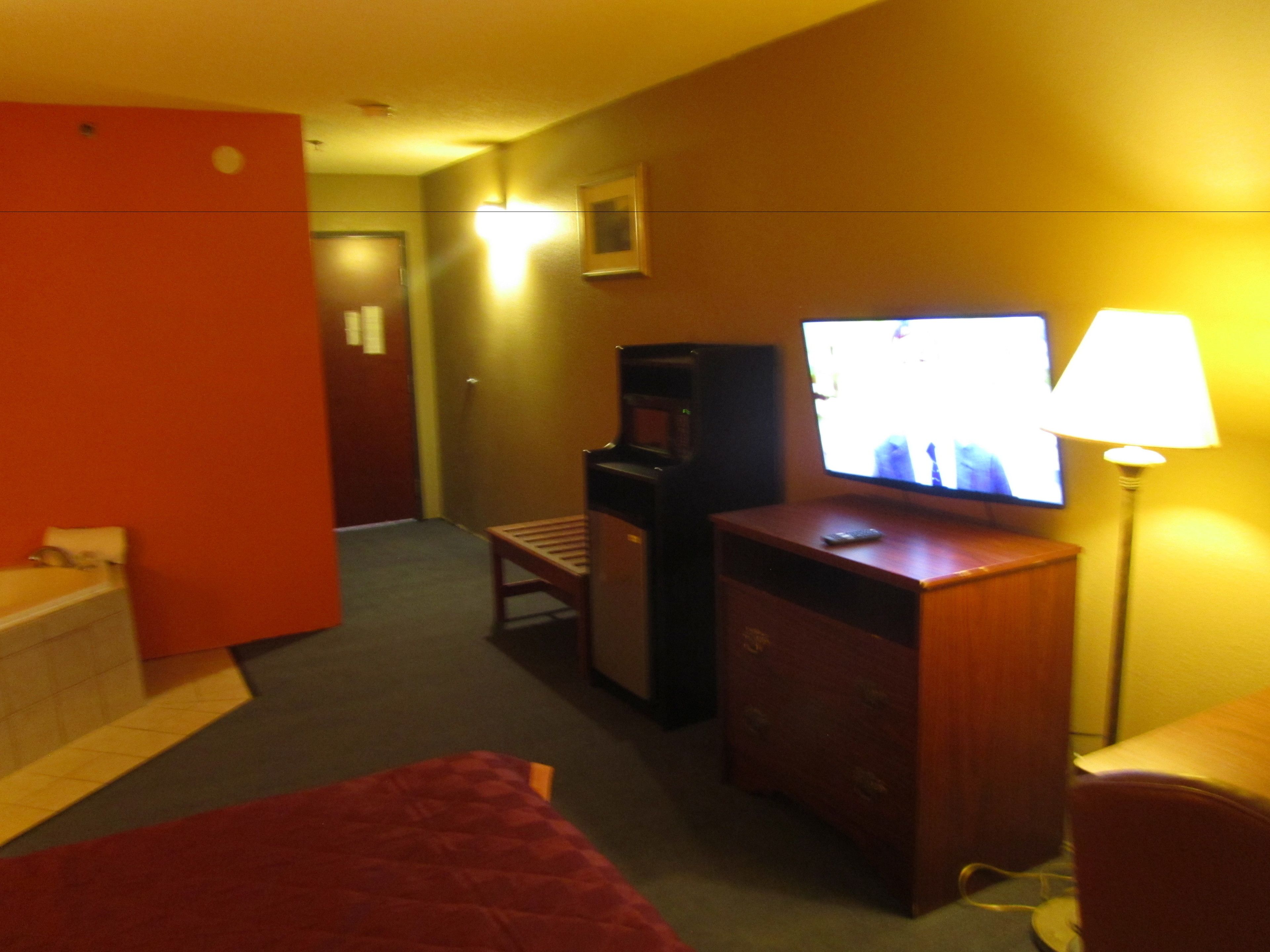 Camera d'albergo con un letto, una scrivania con televisore, una sedia, una lampada e un tavolino.