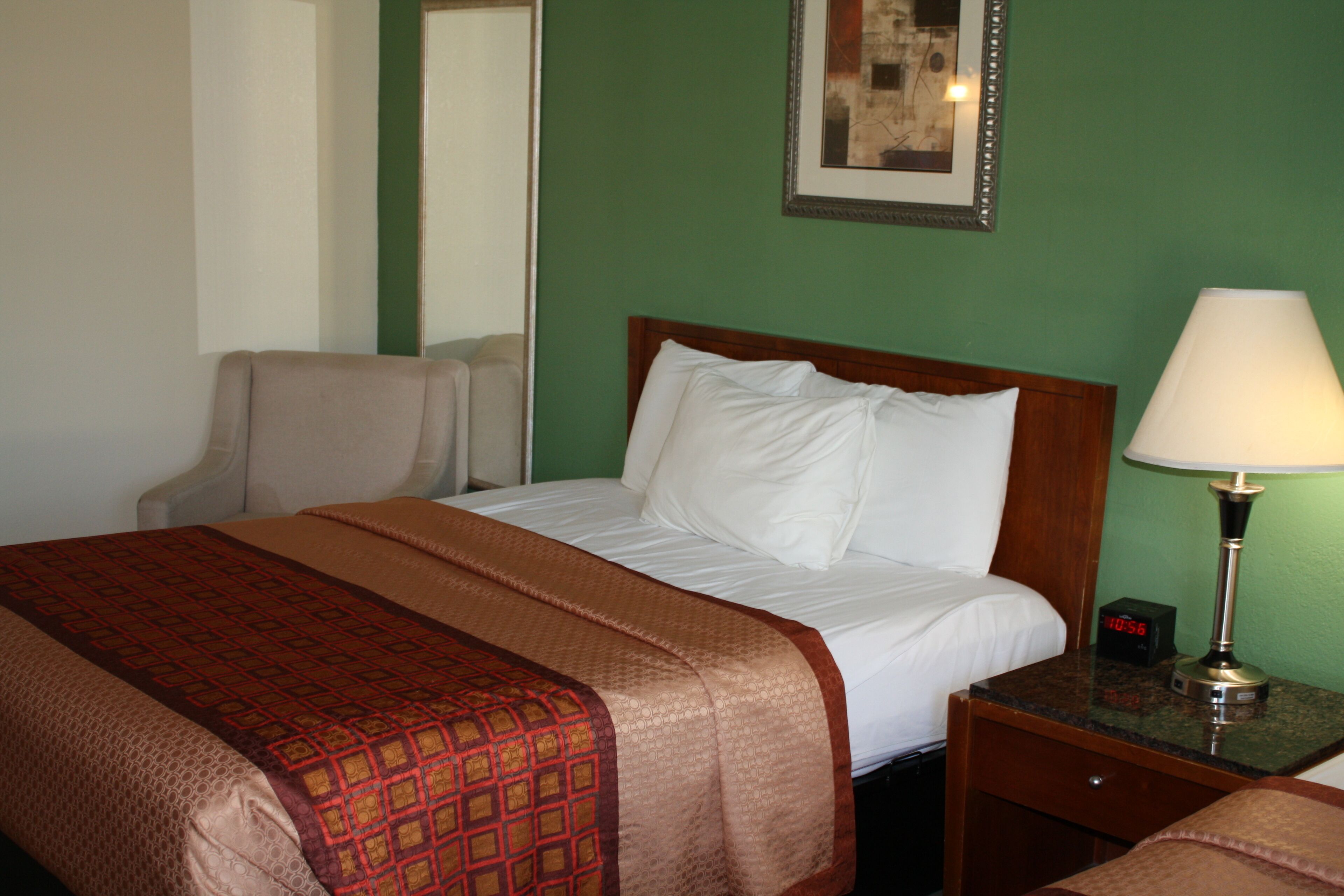 A hotel room with a bed, a nightstand with a lamp, a chair, and a mirror.