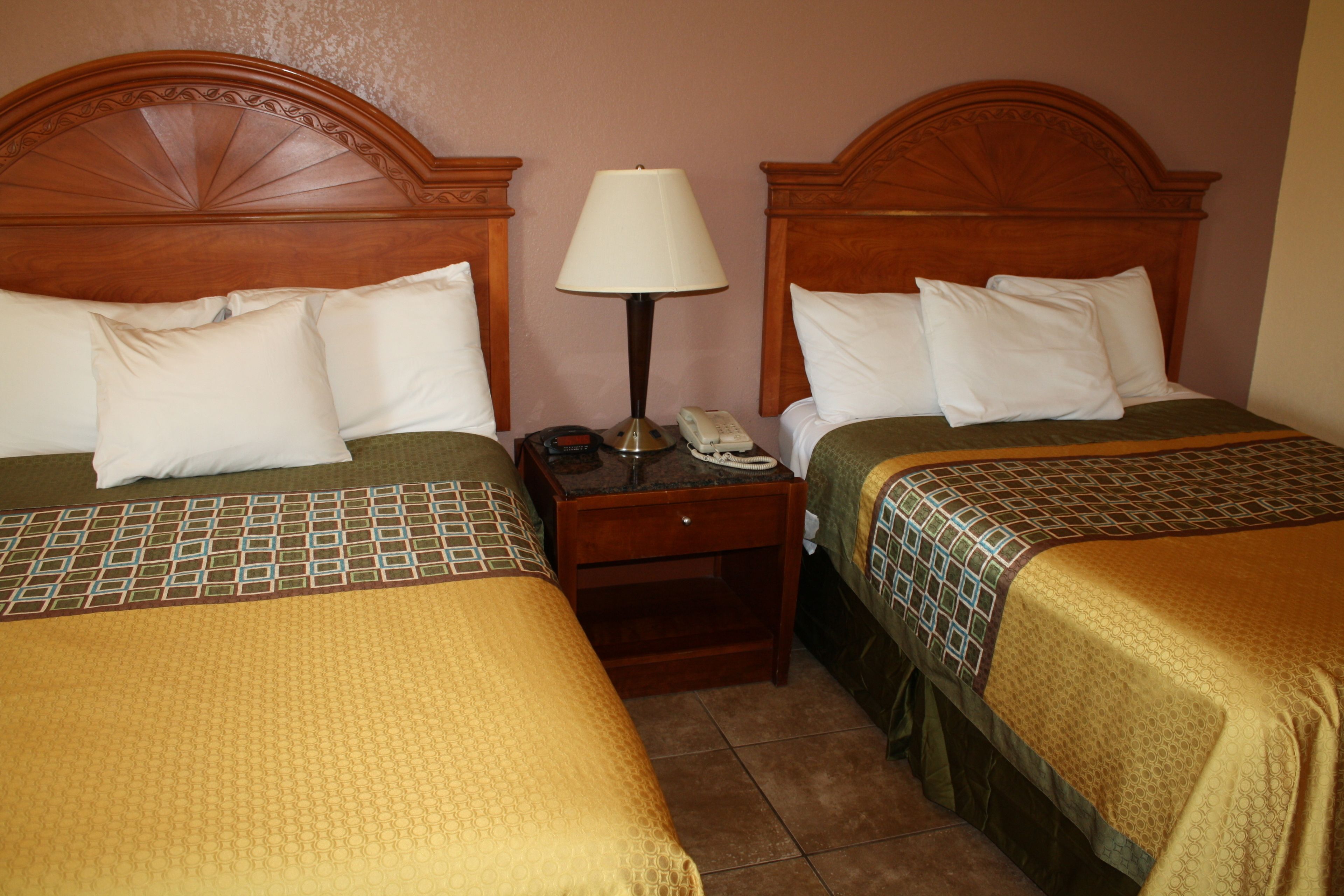 A hotel room with two beds, each with a wooden headboard, a bedside table with a lamp, and a telephone.