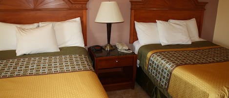 A hotel room with two beds, each with a wooden headboard, a bedside table with a lamp, and a telephone.
