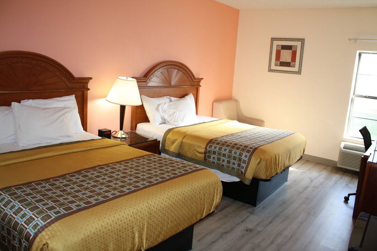 A hotel room with two beds, a nightstand, a lamp, a chair, and a window.