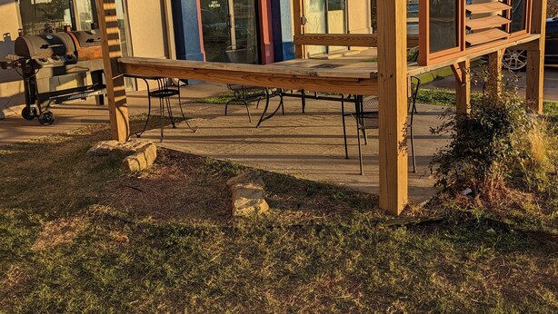 A wooden pergola structure with a bench, a barbecue grill, and a stone planter. - Executive Inn and Suites Wichita Falls (Wichita Falls)