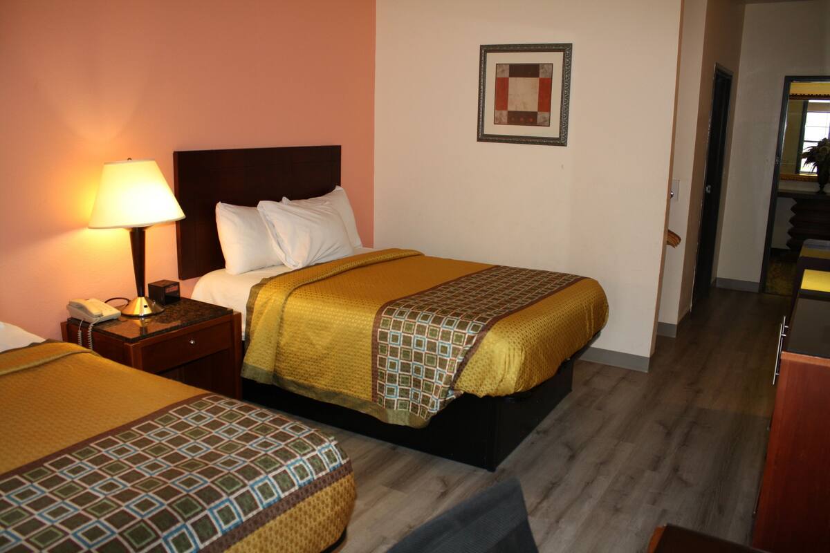 A hotel room with two beds, a nightstand with a lamp, a framed picture on the wall, and a wooden floor.