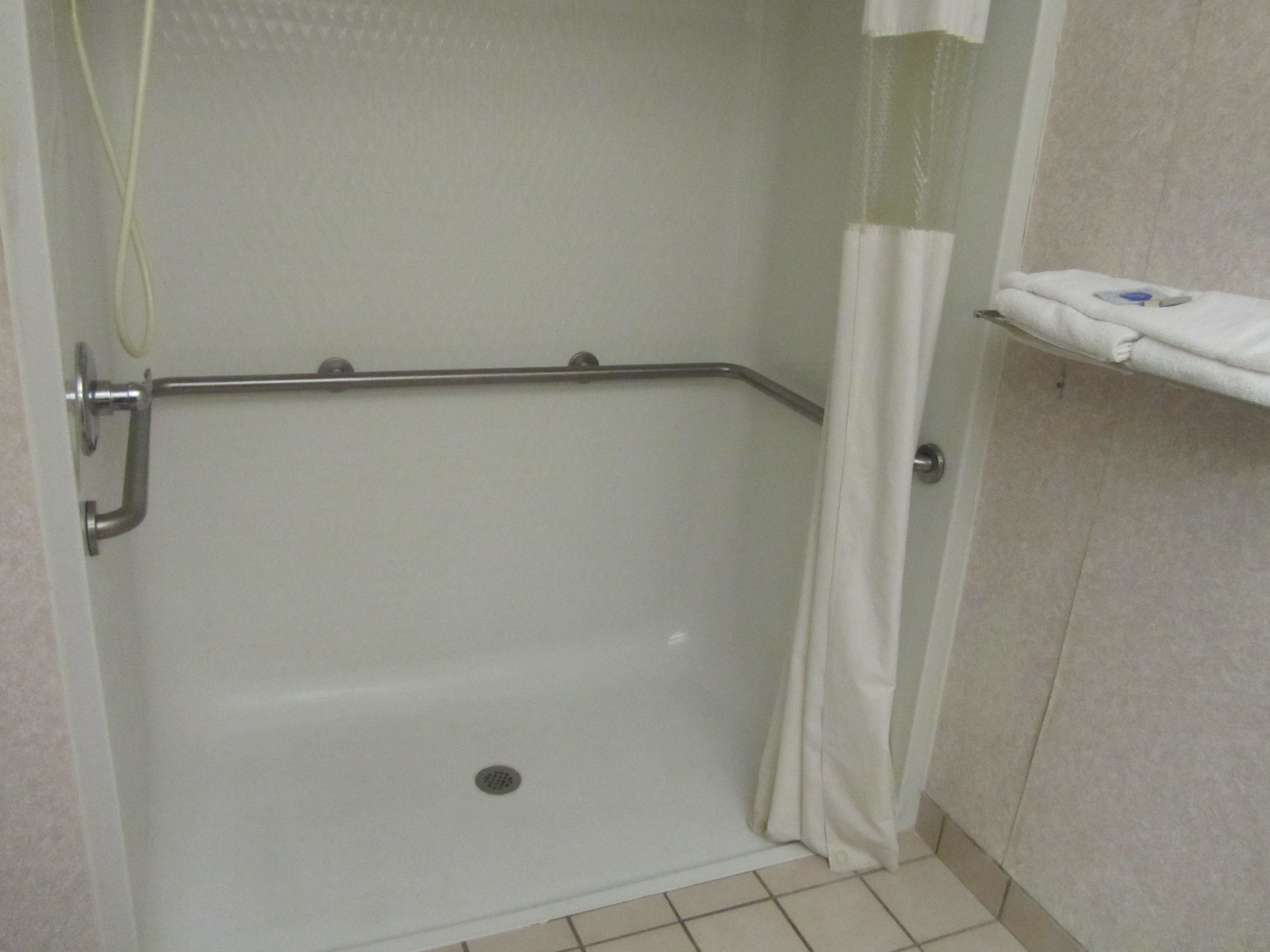 A shower area with a grab bar, a white towel rack, and a tiled floor.