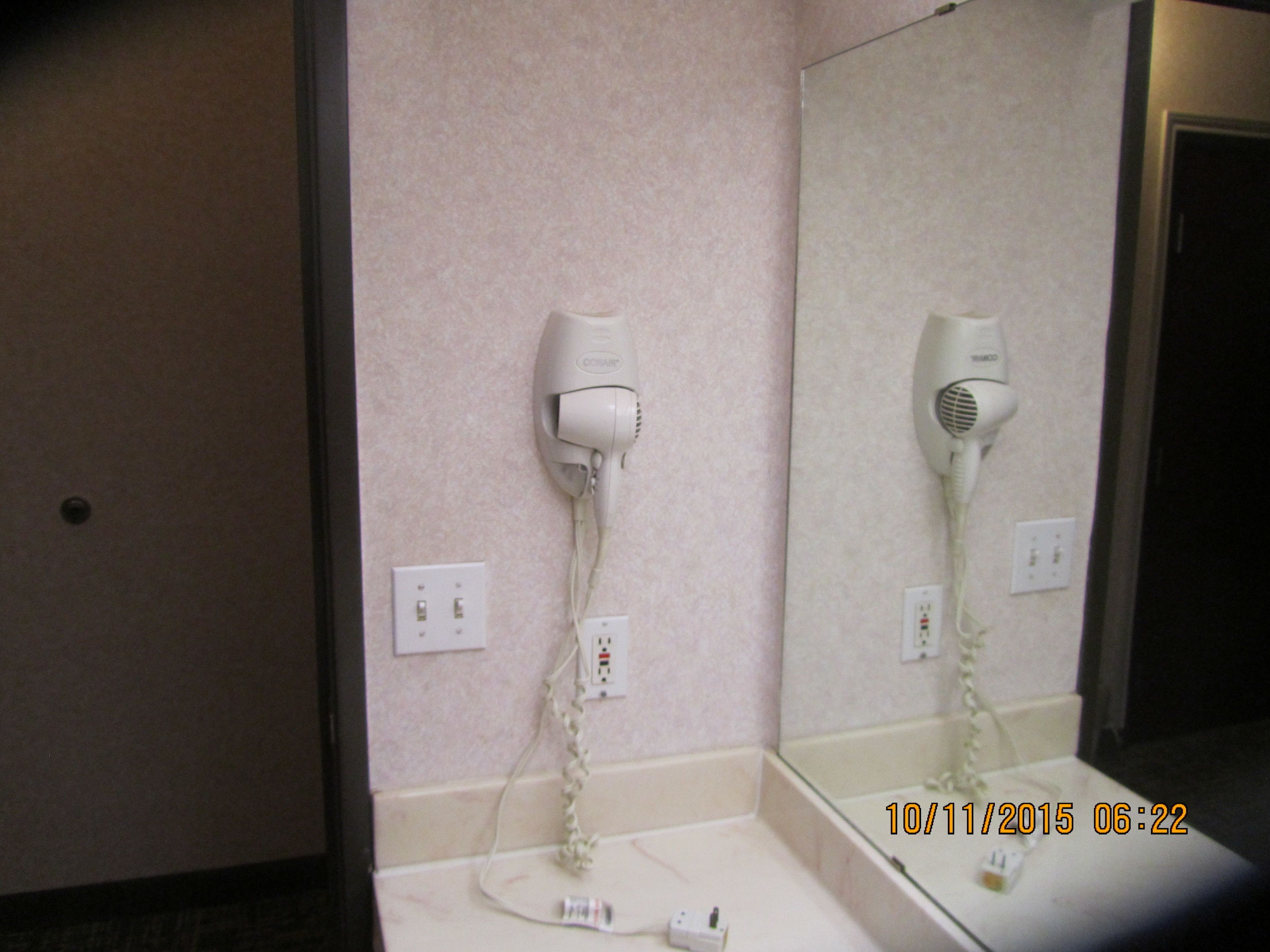 A bathroom with a hairdryer mounted on the wall, a mirror, and a sink.