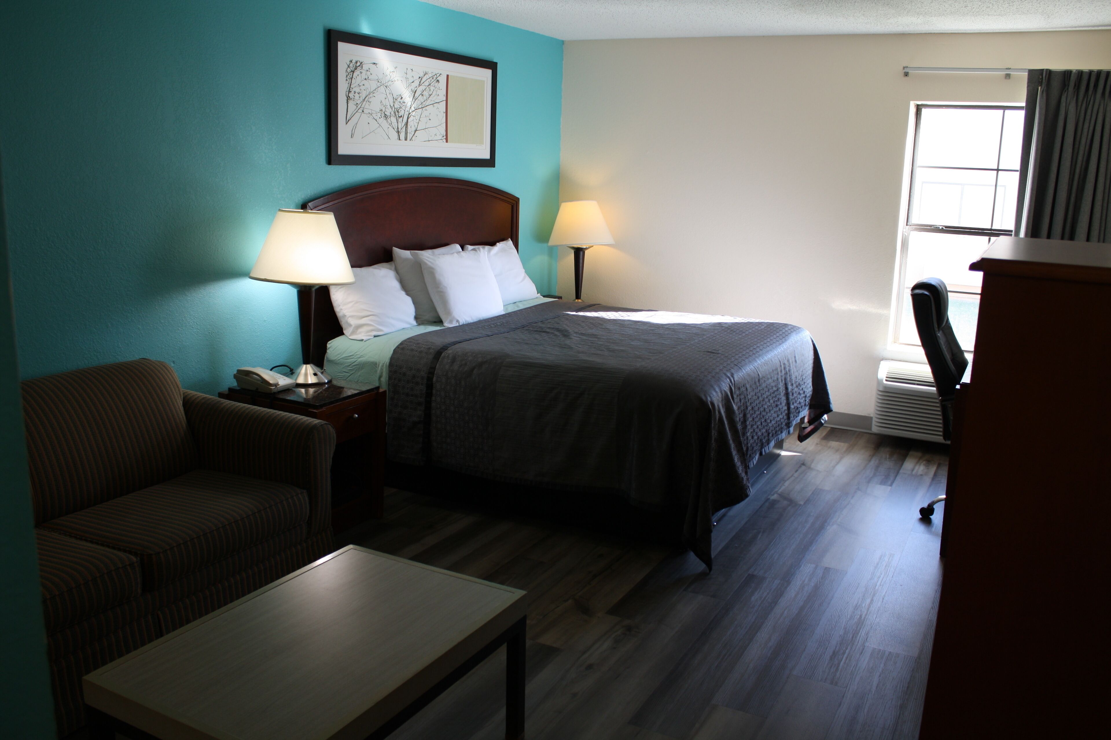 Une chambre d’hôtel avec un lit, deux lampes de chevet, un bureau, une chaise et une fenêtre avec des rideaux.