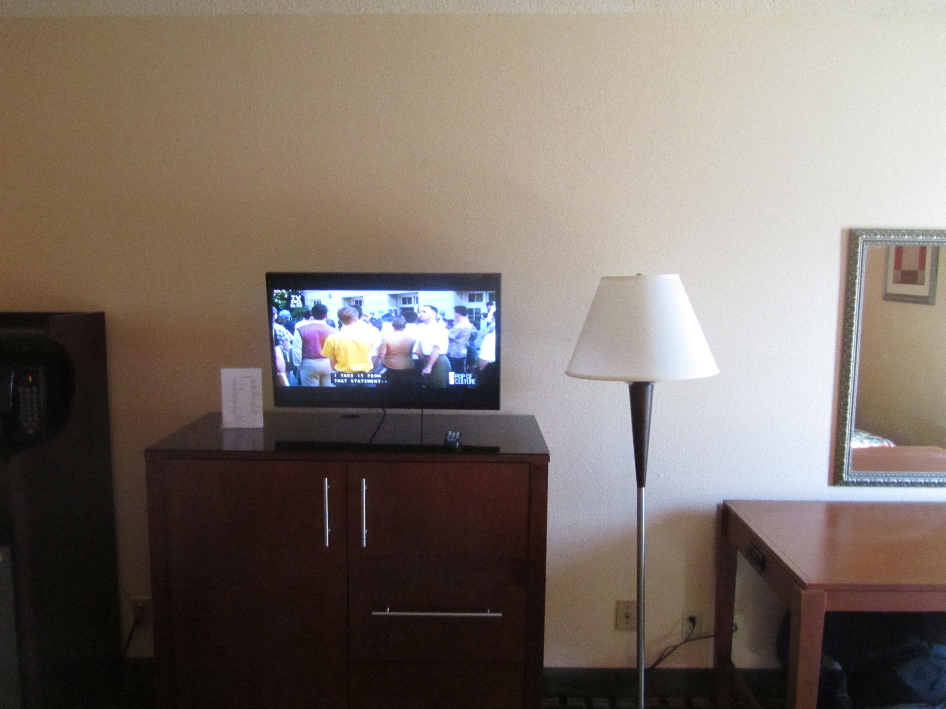 Een televisie op een houten kast, een lamp en een spiegel aan de muur.