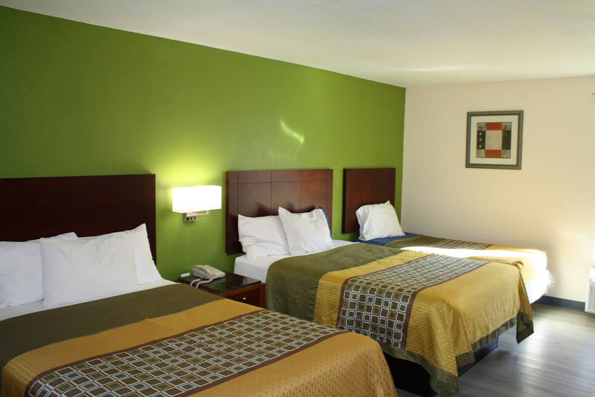 A hotel room with two beds, green walls, wooden headboards, and a framed picture on the wall.